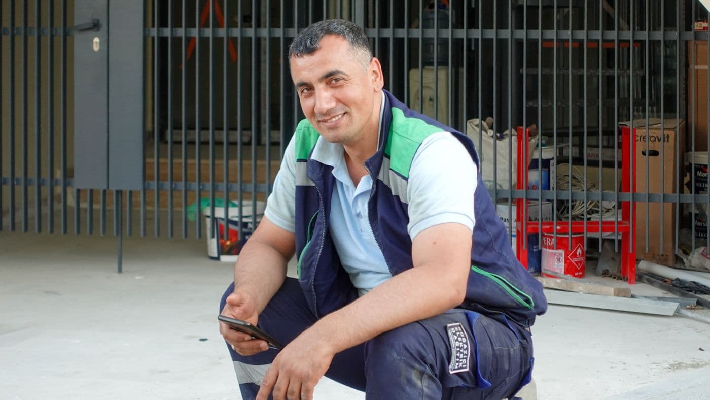 Artisan souriant assis devant son atelier avec son téléphone
